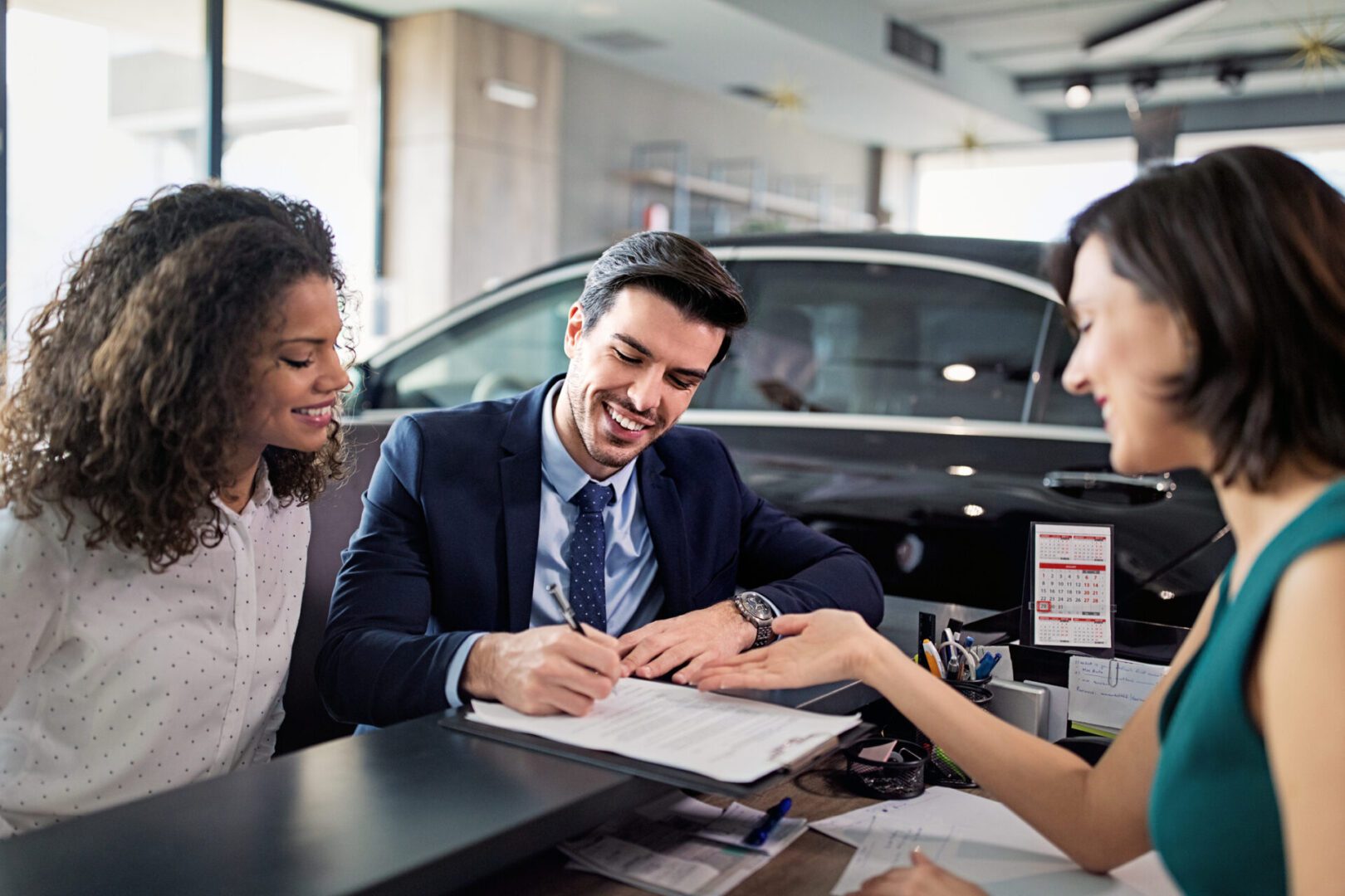 Car dealership transaction with smiling customers.
